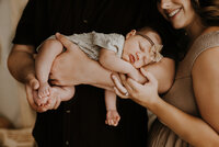 A newborn baby laying across her dad's forearm while sleeping and mom holding her tiny hand in a boho studio in fort worth, texas.