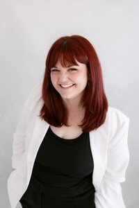 Anna Delores Photography founder, Emily smiles in white blazer and black blouse.