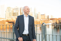 A bald man in a suit posing on a bridge, with a river in the background at an Austin photo studio.