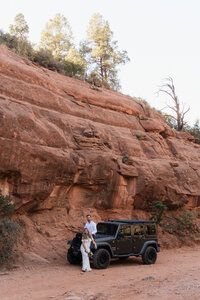 Bride and groom posing beside black Jeep on a red rock trail at Merry Go Round Rock in Sedona during their adventurous desert elopement.