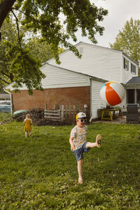 boy kicks classic beach ball into the air while playing in his backyard