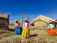 Women in colorful traditional dress with a saturated blue sky and an arch and hut woven from reeds on one of the Taquile Floating Islands in Lake Titicaca, Peru ©Stephanie Dosch | theViatrix Luxury Travel