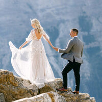 This image depicts a bride holding her groom's hand as they navigate through rocky terrain at the Peyto Lake viewpoint in Banff National Park. The couple’s journey through the rugged landscape symbolizes their commitment to walk through life together, set against the stunning backdrop of the lake's vibrant turquoise waters.