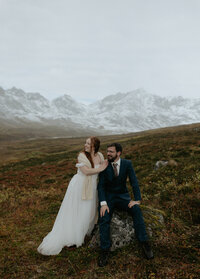 A couple sitting on a rock while surrounded by the mountains. 