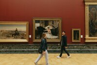 A couple walks past each other in a blurry photoshoot inside of a museum.