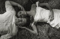 Couple lying in tall grass during elopement photoshoot, bride in simple gown