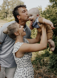 A couple posing with their baby as they smile for a photo
