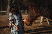 Girl in cowboy hat scratches the nose of a rescue horse during her elopement.