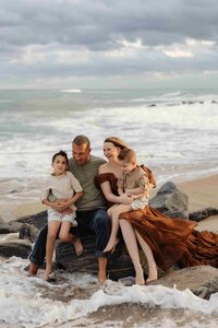 Parents with their 2 kids on the beach sitting on a big rocks