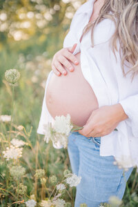 A serene image of a pregnant mother's bare belly, partially covered by an open shirt, standing in a beautiful field. The soft light illuminates the curve of her belly, capturing the peaceful and natural beauty of the moment