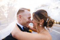 bride and groom holding one another smiling and laughing while touching noses underneath the brides veil in front of the united states capitol building 