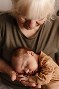 Grandmother lovingly cradling a sleeping newborn in her hands during an in-home lifestyle session in Las Vegas — natural light, emotional connection captured by Angela Wolf Photography