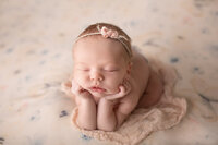 Baby safely posed on a pink watercolor backdrop during her newborn session.