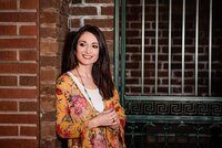 Woman wearing a yellow flower print dress leaning against a brick wall