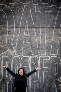 A person in black clothing stands with arms outstretched in front of a large mural with text, embodying the spirit of educational leadership.