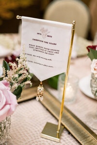 Gold-framed fabric sign with personal couple trivia displayed as a unique wedding centerpiece.