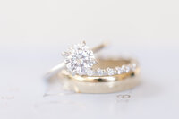 Bride’s wedding rings delicately stacked on top of the groom’s ring, symbolizing unity, love, and the intertwined journey of marriage.