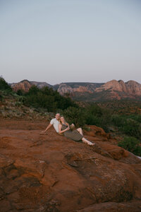 A couple sit snuggled up together among red rocks in Sedona