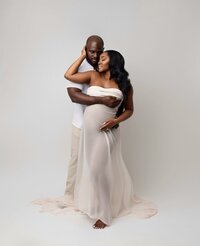 Pregnant couple posing for photo with mom wrapped in sheer cloth.
