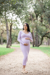 Expectant mother gently cradling her baby bump while gazing thoughtfully into distance during San Jose oak grove maternity session