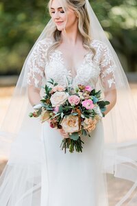 Bride holding bouquet in lace and a veil. Detail photo of bride with soft peach and pink flowers