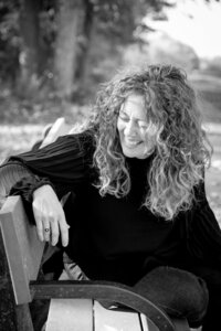 black and white headshot of woman sitting and laughing on bench in park