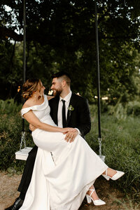 bride and groom sitting on a tree swing