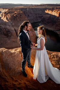 A couple standing at the edge of Horseshoe Bend, holding hands during their intimate elopement ceremony with stunning views of the canyon.