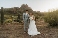 A newlywed couple standing in a desert looking at each other and smiling 