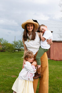 mom holds her son and daughter hugs her as she looks toward camera with red barn in background