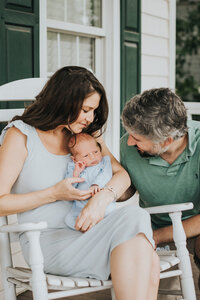 Couple holds and smiles at baby boy on front porch during newborn session in Raleigh