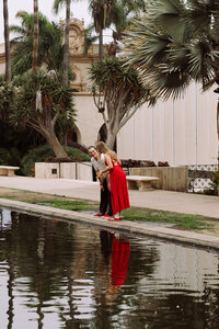 couple standing over pond, sharing special moment, woman in red dress