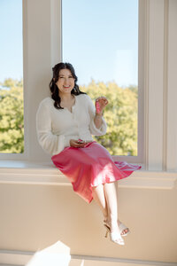 Shanté Gorman, founder of Sugarpunch Marketing®, sitting by a window in a pink skirt, representing her content marketing agency.