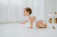 Baby girl in white outfit crawls in white studio space during baby photography session