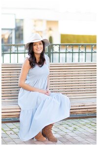 Woman wearing pastel blue dress and cream colored hat sits on park bench for boutique branding photoshoot in the  spring