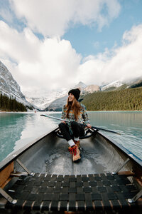 Adventure elopement photographer Meg paddling a canoe on a turquoise mountain lake in Banff, smiling with snow-capped peaks in the background.