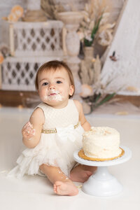 one year old girl smashing cake for first birthday photoshoot