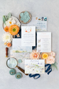 Invitation flatlay for Vail wedding, highlighting vintage stamps, watercolor elements, and weekend details card