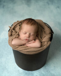 Newborn girl sleeping in pail with blue background.