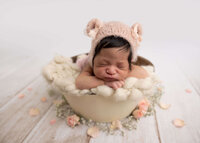 baby girl posed in a cream bucket with a bear beanie.