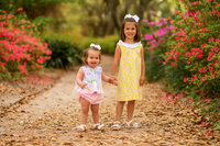 Sisters hold hands among azalea blossoms in Hampton Park during their Family Photoshoot in Charleston.