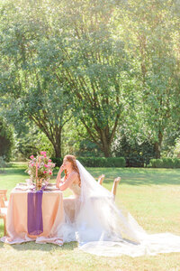 The bride sits down at her pink and purple wedding table.