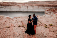 A couple on the shores of Lake Powell, with one partner kneeling to propose, surrounded by the serene beauty of the lake and desert landscape.