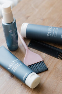 an image of three Eufora hair products in dusty blue bottles on a wooden table with a comb and brush to apply color