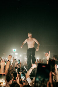 Dynamic event photography capturing Sam Hofman performing shirtless on stage in front of an energetic crowd at a club in Tilburg, by Bo Eppink.