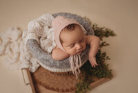 Newborn baby boy, asleep,  propped on hands in basket with one hand on cheek and wearing a green sleepy cap