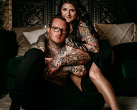 Tattooed woman and man kissing outdoors in front of green trees