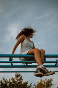 A person sits atop a blue structure, hair tossed by the wind against a serene sky, hinting at freedom and spirited energy.