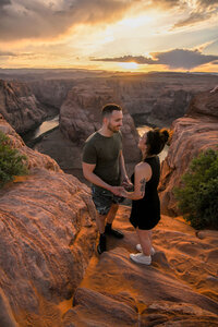 A man down on one knee proposing at Horseshoe Bend, with the winding Colorado River and sweeping desert landscape in the background.