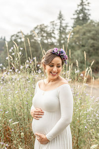 Pregnant woman in nature wearing a white off the shoulder maternity dress for her maternity portraits.